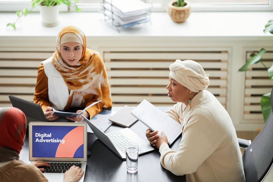 Three women collaborating on digital advertising strategies around a table with laptops.